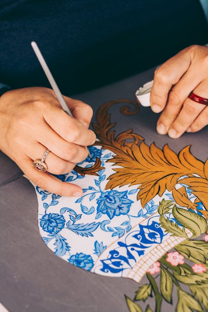 Close-up of skilled hands painting intricate floral patterns on pottery, showcasing craftsmanship.